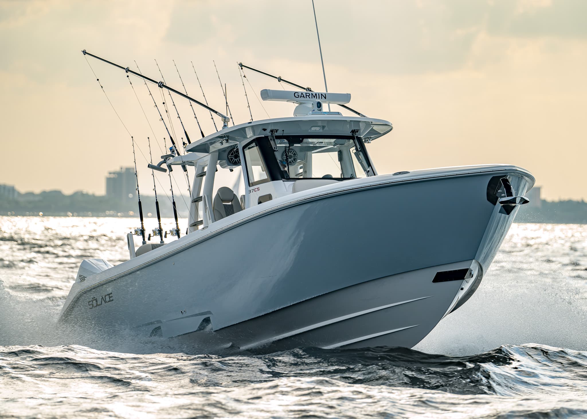 A white Solace 37 CS center-console fishing boat speeds across choppy water with multiple fishing rods mounted at the back.